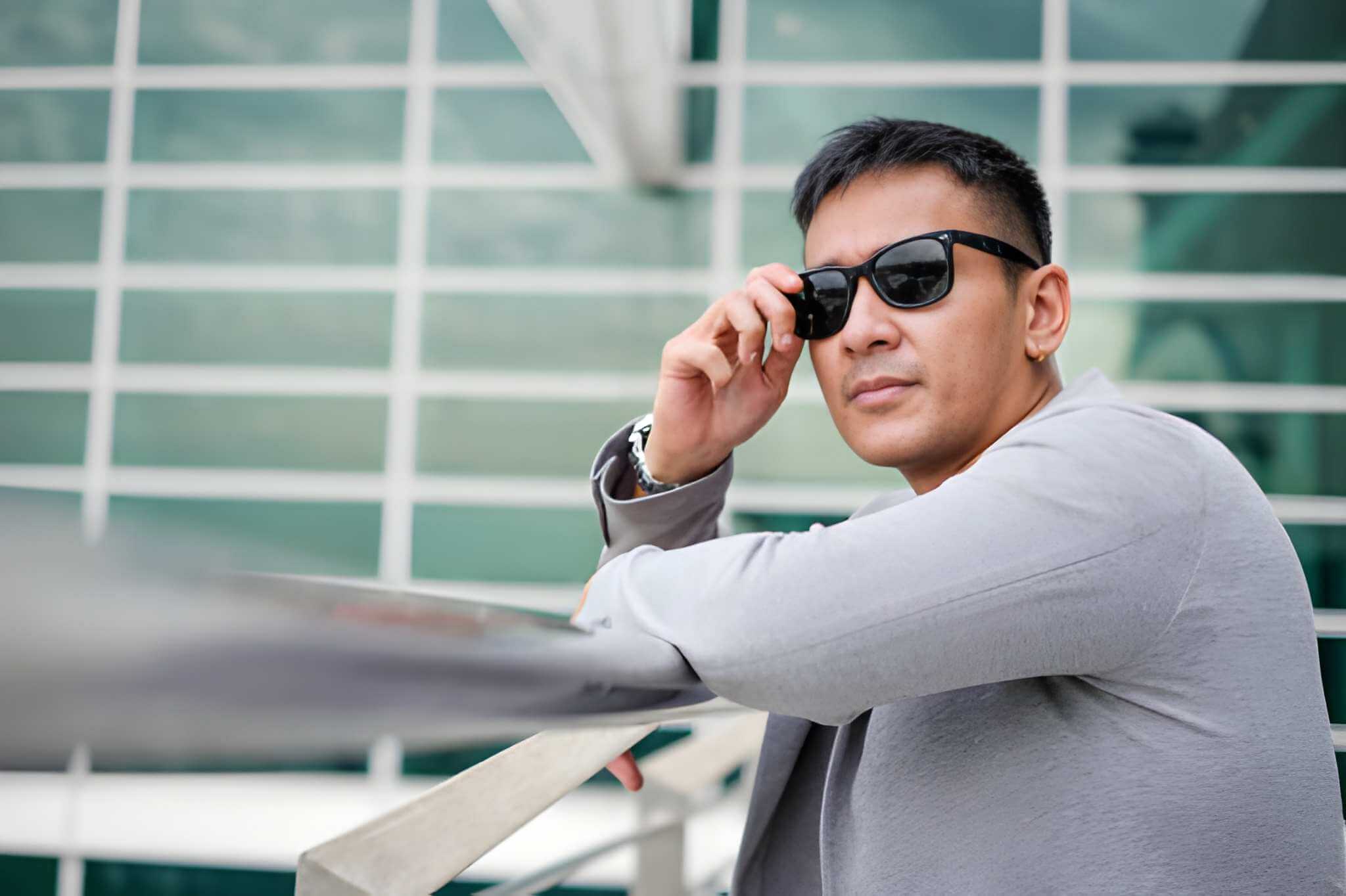 Man adjusting sunglasses in front of a modern building